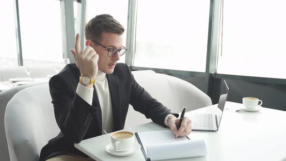 Elegant Dressed Male in Eyeglasses Writing Business Plan Taking Notes While Sitting at Table in