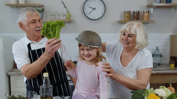 Senior Woman and Man with Grandchild Girl Fooling Around with Strainer and Vegetables at Home alt