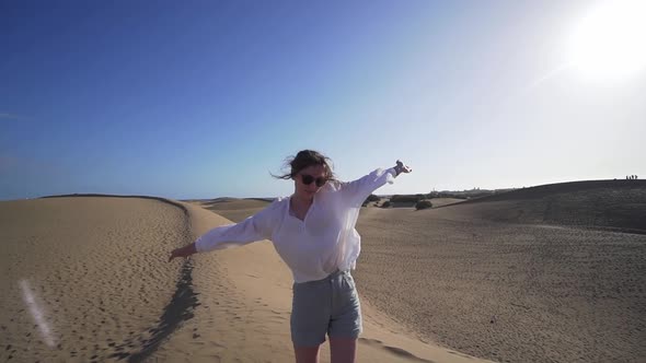 Attractive Young Woman in a White Shirt and Glasses in the Desert on a Dune Whirls Around Herself