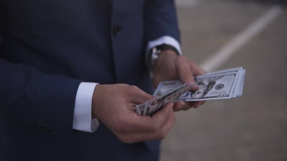 Unrecognizable Businessman on the Street Holding Bundle of American Money in His Hands Counting It alt