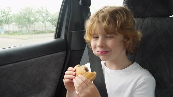 Blonde hungry boy eating a delicious cheeseburger in the car.