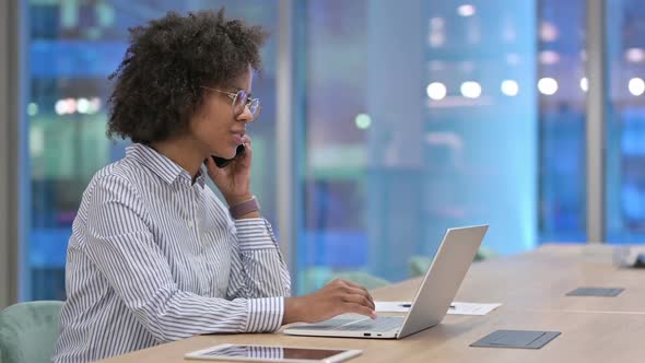 African Businesswoman with Laptop Talking on Smartphone in Office alt