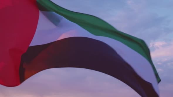 Close-up of the flag of the United Arab Emirates waving in the wind against a cloudless blue sky.
