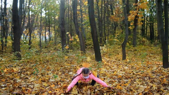 A little girl in a medical mask throws fallen yellow leaves in a Park on an autumn day.