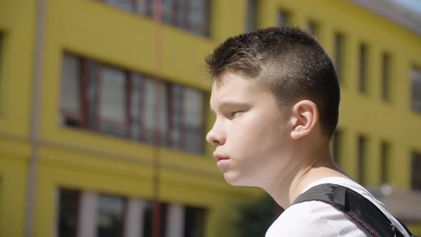 A Caucasian Teenage Boy Looks Around  Closeup  a School in the Background