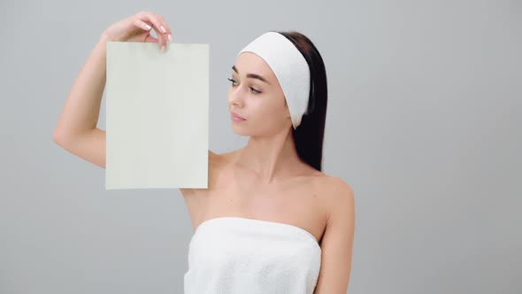 A young beautiful woman in a headband and a bath towel shows a white sheet. alt