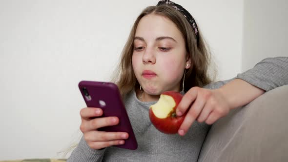 Teen Girl Eating Apple While Chatting on Smartphone Childhood alt