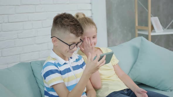 Close Up of an Excited Twins Kids Using Smartphone Sitting Together on Sofa alt