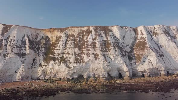 Drone flies low away from the White Cliffs of Dover, revealing beautiful turquoise sea in the foregr alt