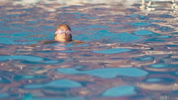 A Girl in a Bright Swimsuit with Swimming Goggles Dives Into a Pool with Clear Transparent Water alt