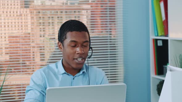 Close-up of Black Man in Headset Speaking with Somebody and Working on the Computer