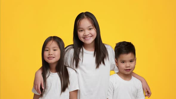 Happy Asian Girl Hugging Little Brother And Sister Yellow Background alt