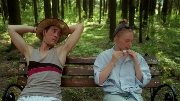 A Guy in a Straw Hat and a Girl in a Blue Shirt Sit on a Bench in the Woods