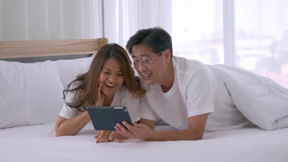 Happy senior couple using tablet computer together on the bed alt