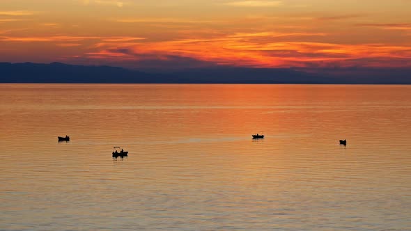 Small Boat Silhouettes On Calm Sea At Sunset
