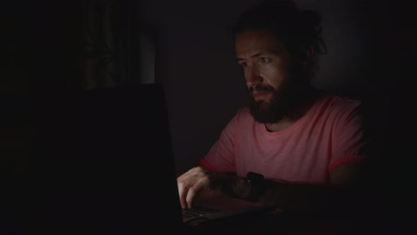 Young Bearded Man Working on Laptop in Darkness