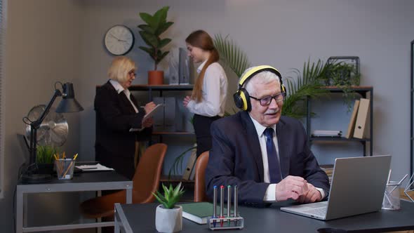 Cheerful Senior Business Man Working on Portable Laptop Sitting at Desk Listening Music and Dancing alt
