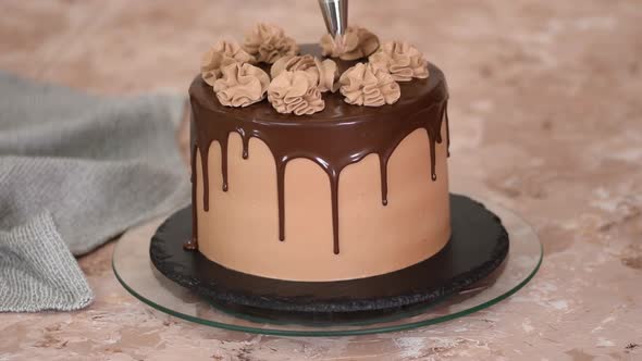 Female hands decorate a sponge cake with chocolate cream from a pastry bag.
