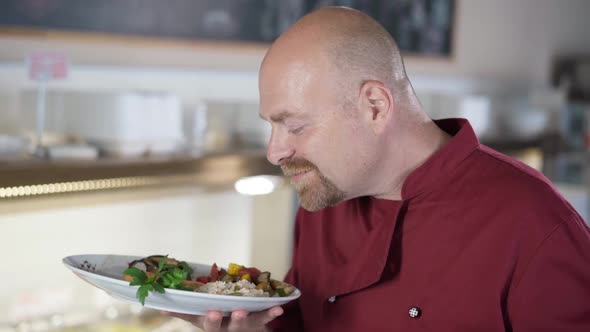 Satisfied Male Cook Smelling Delicious Dinner on Plate Looking at Camera Smiling alt
