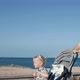 Young Woman with Daughter in a Stroller is Walking Along the Promenade By Sea - VideoHive Item for Sale