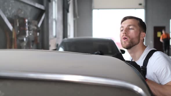 A Car Mechanic Blows Dust From a Retro Car That is Broken in the Garage alt