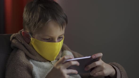 Teen Guy in a Protective Mask with a Phone in His Hands. Coronavirus Epidemic 2020.