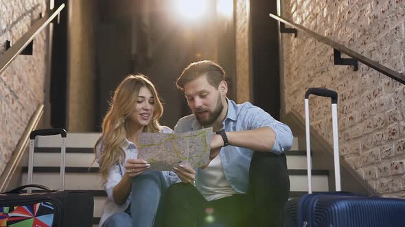 Cheerful 30s Pair in Love which Sitting on Stairs and Using Map Talking alt