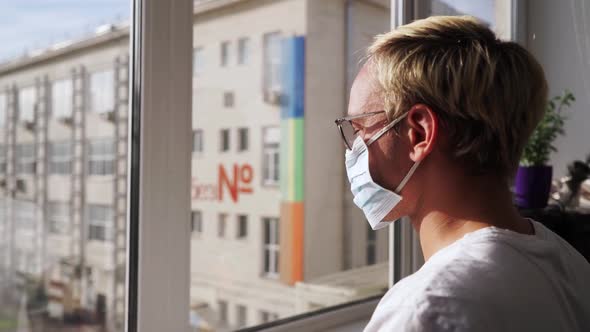 Man Wearing a Protective Medical Mask Looking Out of the Window During Quarantine. Home Isolated