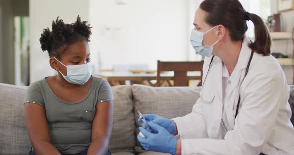 African american girl and caucasian female doctor wearing face masks, vaccinating alt