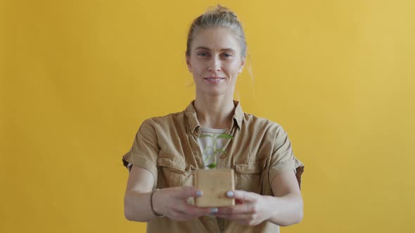 Young Woman Holding Little Sprout Plant and Smiling Protecting Nature on Yellow Background alt