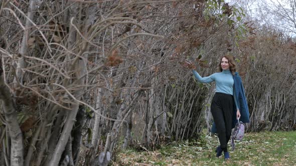 Young Redhaired Woman in a Blue Coat and Walks Against the Backdrop of the Old City alt