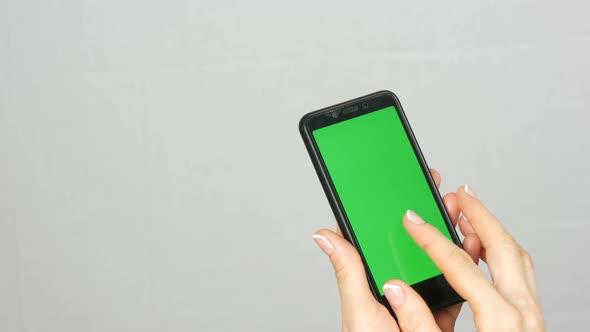 Wellgroomed Neat Female Hands with a Beautiful Manicure Hold a Black Smartphone with a Green Screen alt