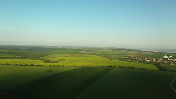 Aerial Descent Over Green Fields with Clear Blue Sky, Moon, Road and Small Town in the Background alt