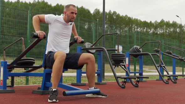 Man Trains in the Air on a Simulator Does Triceps Exercises alt