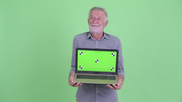 Happy Senior Bearded Man Thinking While Showing Laptop alt