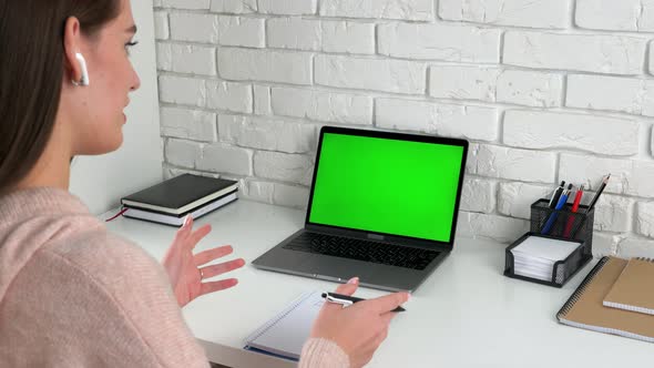 Woman teacher with pen in hand communicates talk speak with green screen laptop alt