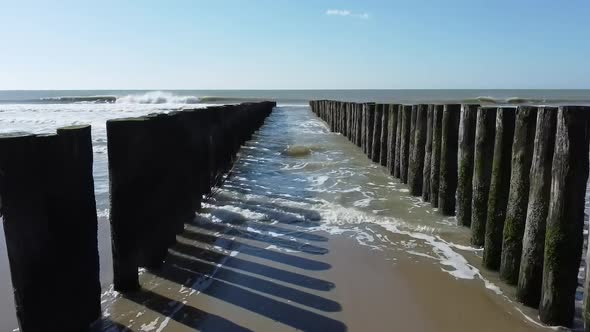 Flying with a drone towards the sea and the blue sky between a double breakwater. alt