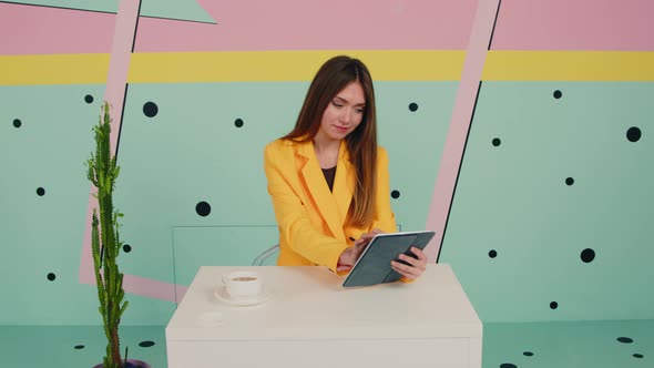 Woman In Yellow Jacket Uses Tablet Computer and Looks at Camera
