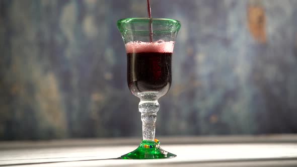 Seamless, looping clip of red wine pouring into a rustic glass with blue background. alt