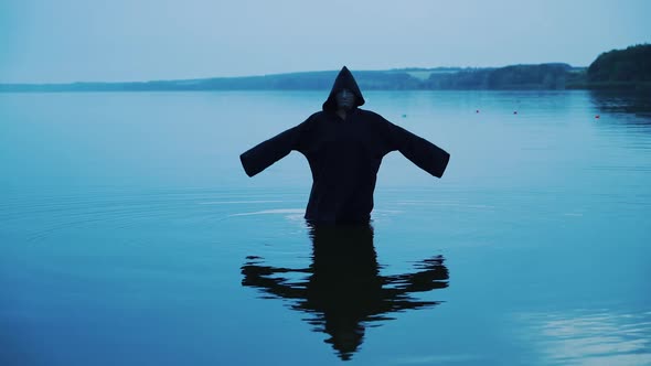 Terrible figure in a black robe in the water outdoor. Divination by Halloween alt