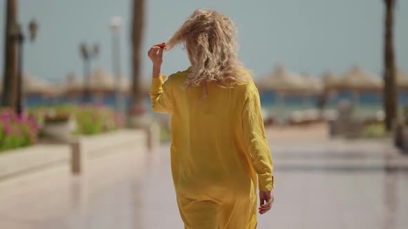 a Curly Blonde in a Yellow Fluttering Dress Goes to the Beach with Umbrellas on a Sunny Day alt