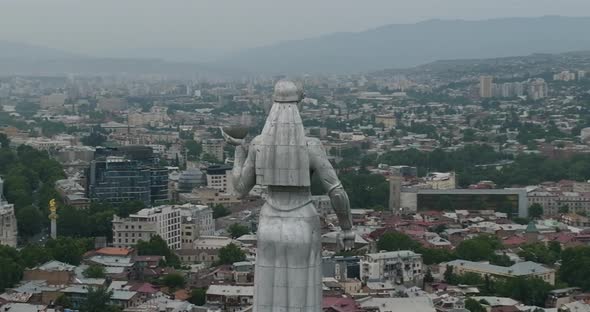 Arc aerial shot of the Kartlis Deda statue with Tbilisi cityscape in the back. alt