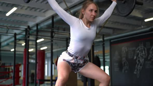 Slim Concentrated Sportswoman Squatting with Heavy Barbell in Slow Motion Indoors alt
