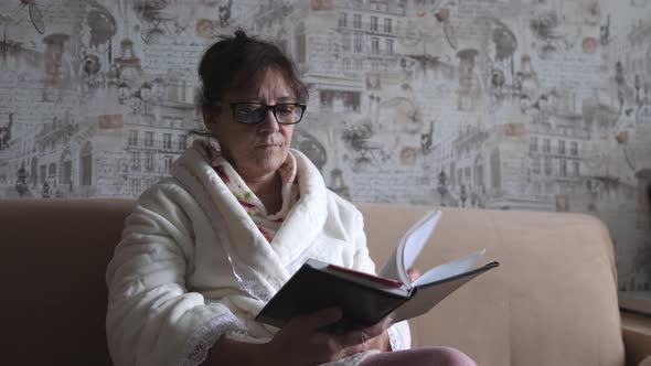 Middle Aged Woman in Glasses Flipping Through Paper Book Reading Fascinating Story