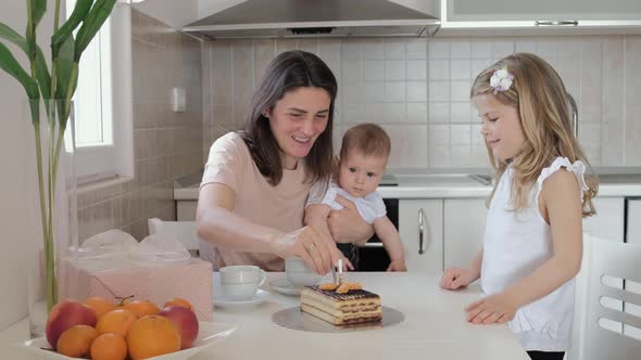 First birthday, mother lights a candle on the cake at home. Friends meet on a holiday with kids alt