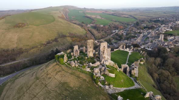 Amazing view of Corfe Castle perched on hill during golden hour. Aerial circling alt