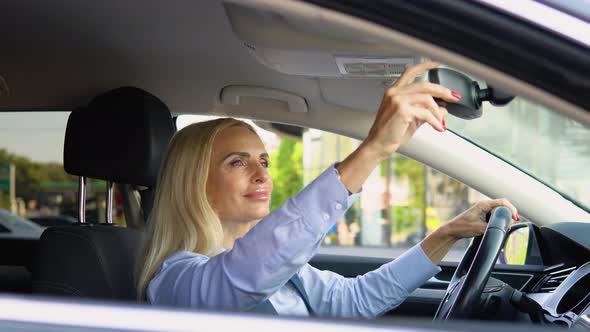 Elegant Senior Woman Looks at the Car Mirror of Her Car Near Modern Office Building alt