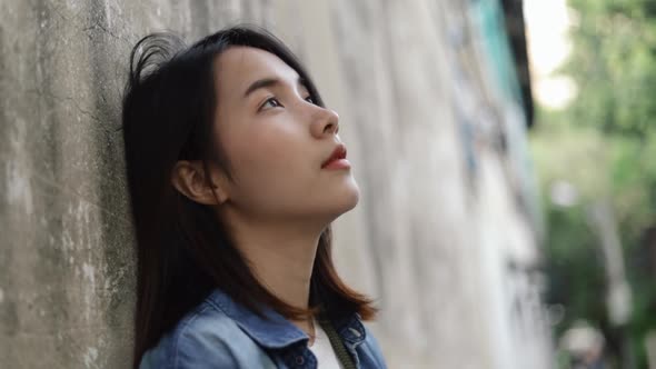 Beautiful young Asian female loneliness feeling leaning against the wall at a small street.