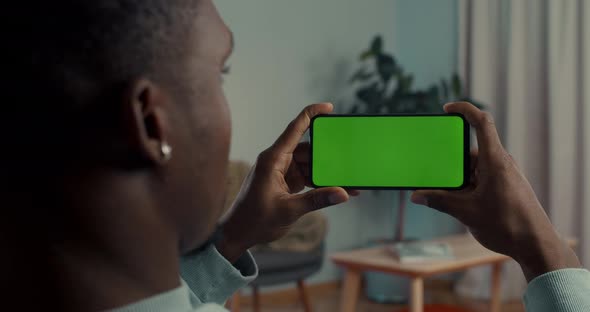 View From Shoulder of African American Guy Using Cell Phone with Green Mock Up Screen While Sitting alt