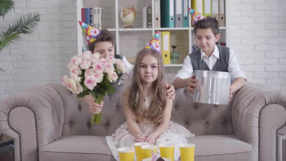 Portrait of Pretty Little Caucasian Girl in Party Hat Receiving Bouquet of Roses and Gift Box From alt